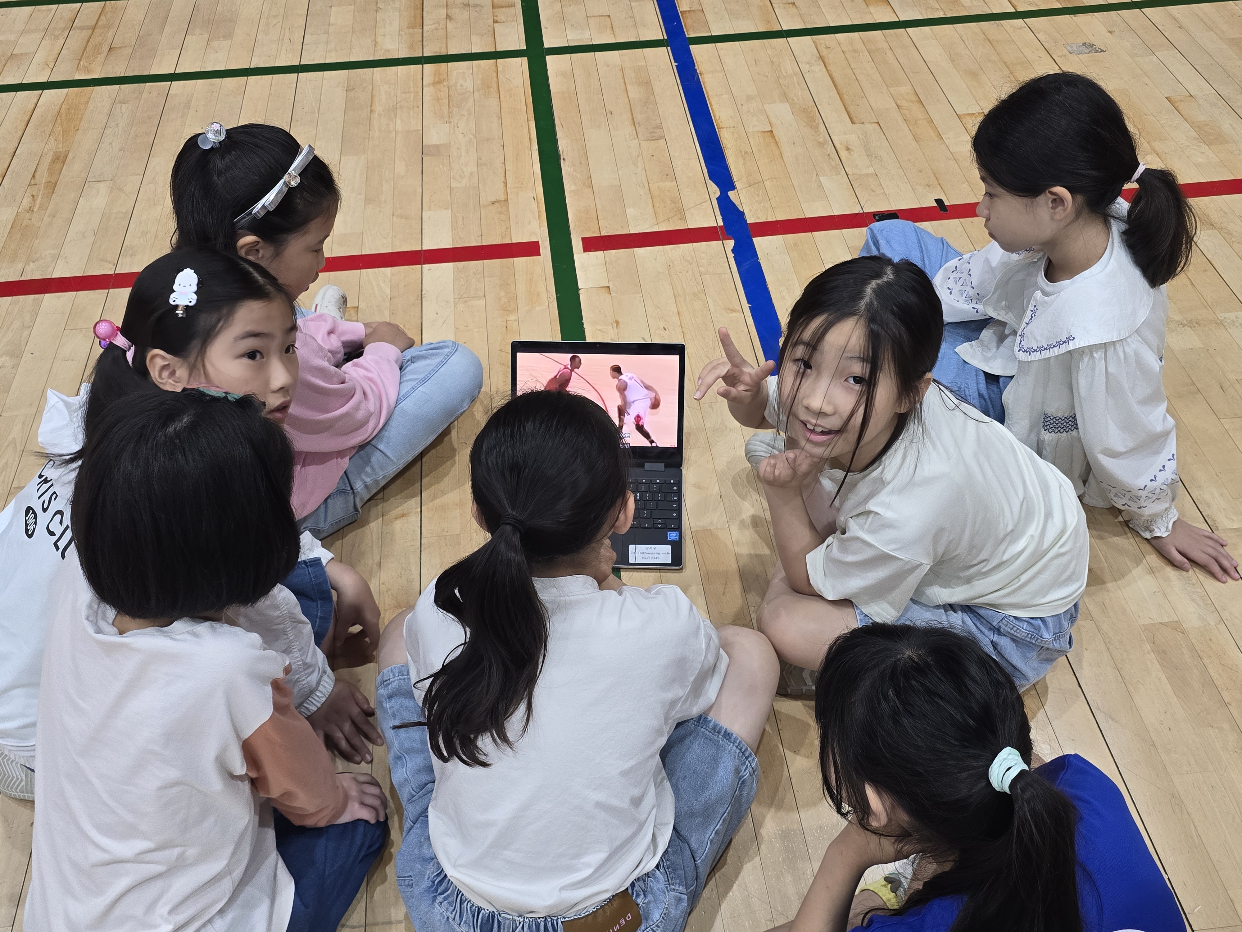7. 체육관에 옹기종기 모여 앉아 태블릿 영상을 보며 올바르게 공을 튀기는 방법을 다 함께 확인해요.